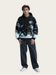 Person wearing a black hoodie with abstract design and dark pants on a beige background