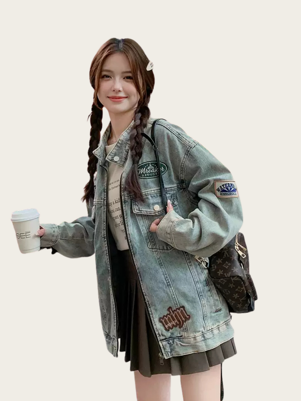 Woman wearing a denim jacket with brand logos, holding a cup and a bag on a plain background