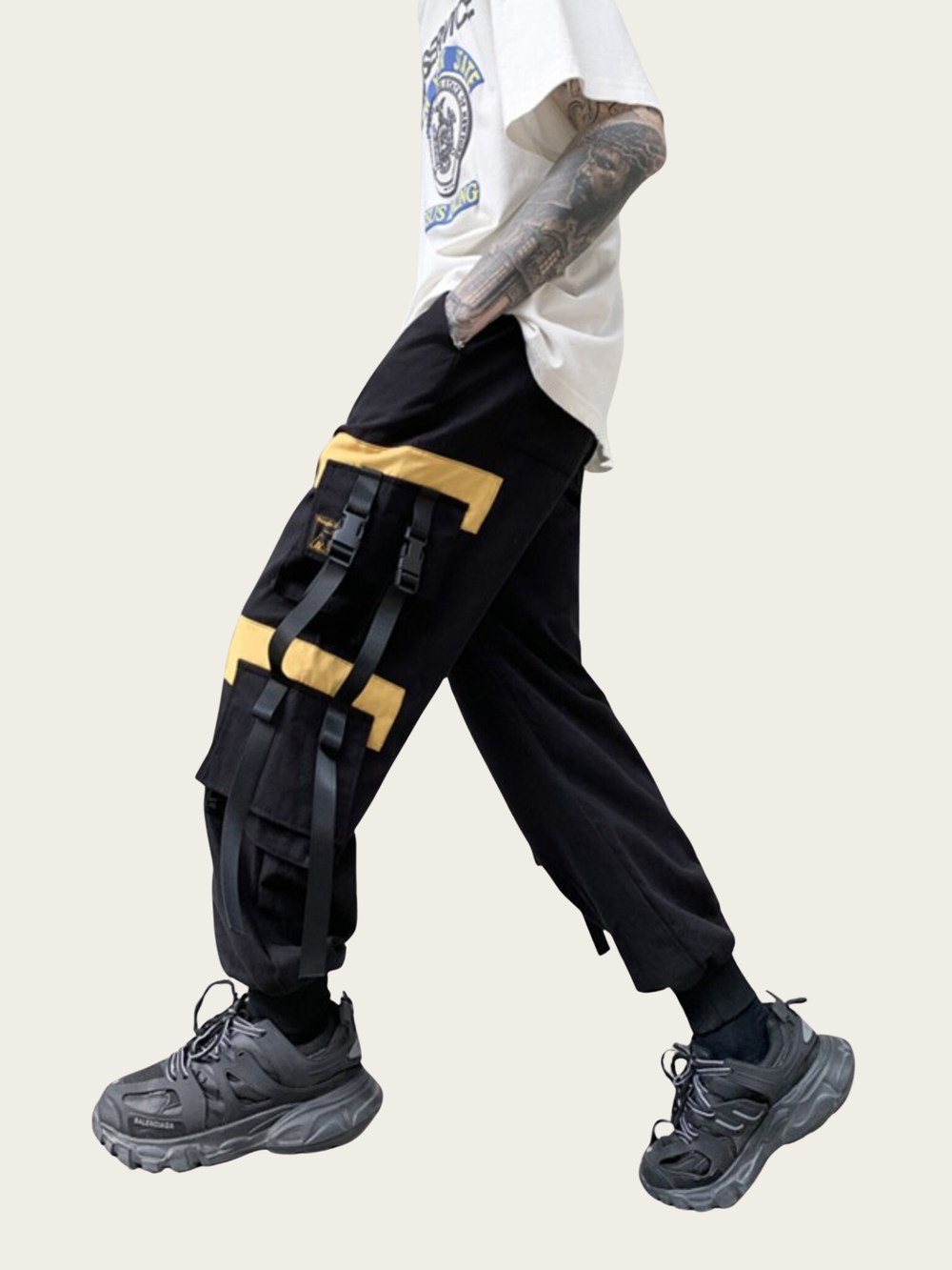 Person wearing black cargo pants with yellow accents and gray sneakers on a light background