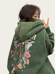 Person wearing a green hoodie with floral designs, covering their face.