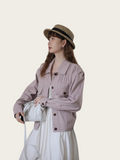 Woman wearing a light purple jacket and white dress with a straw hat on a plain background