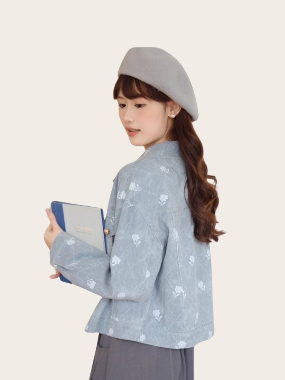 Woman wearing a light blue patterned jacket and gray hat holding a blue clutch against a white background