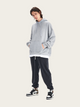 Person wearing a gray hoodie and black pants on a white background