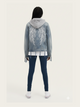 Person wearing a denim jacket with angel wings on the back, standing against a white background