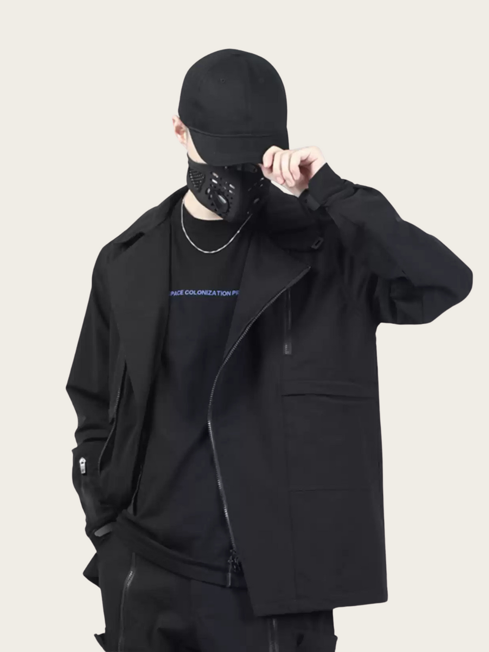 Person wearing a black outfit with a jacket and cap on a plain background