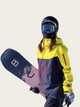 Person wearing a yellow and gray jacket with a blue helmet and goggles, holding a snowboard.