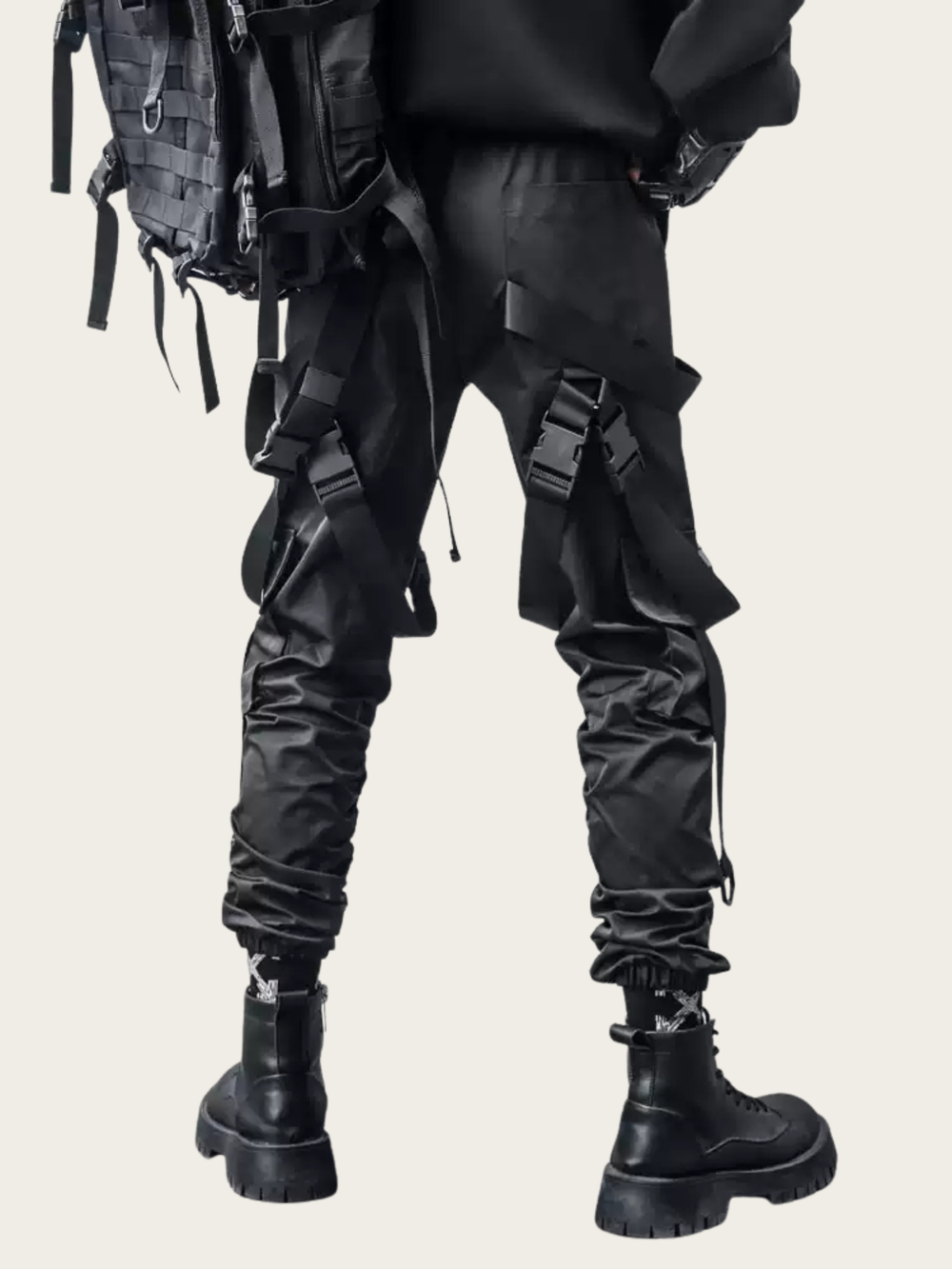 Person wearing black tactical pants with straps and a backpack on a beige background