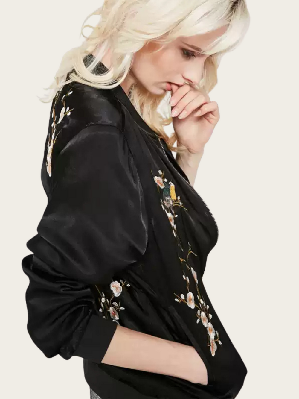 Woman wearing a black jacket with floral embroidery on a plain background