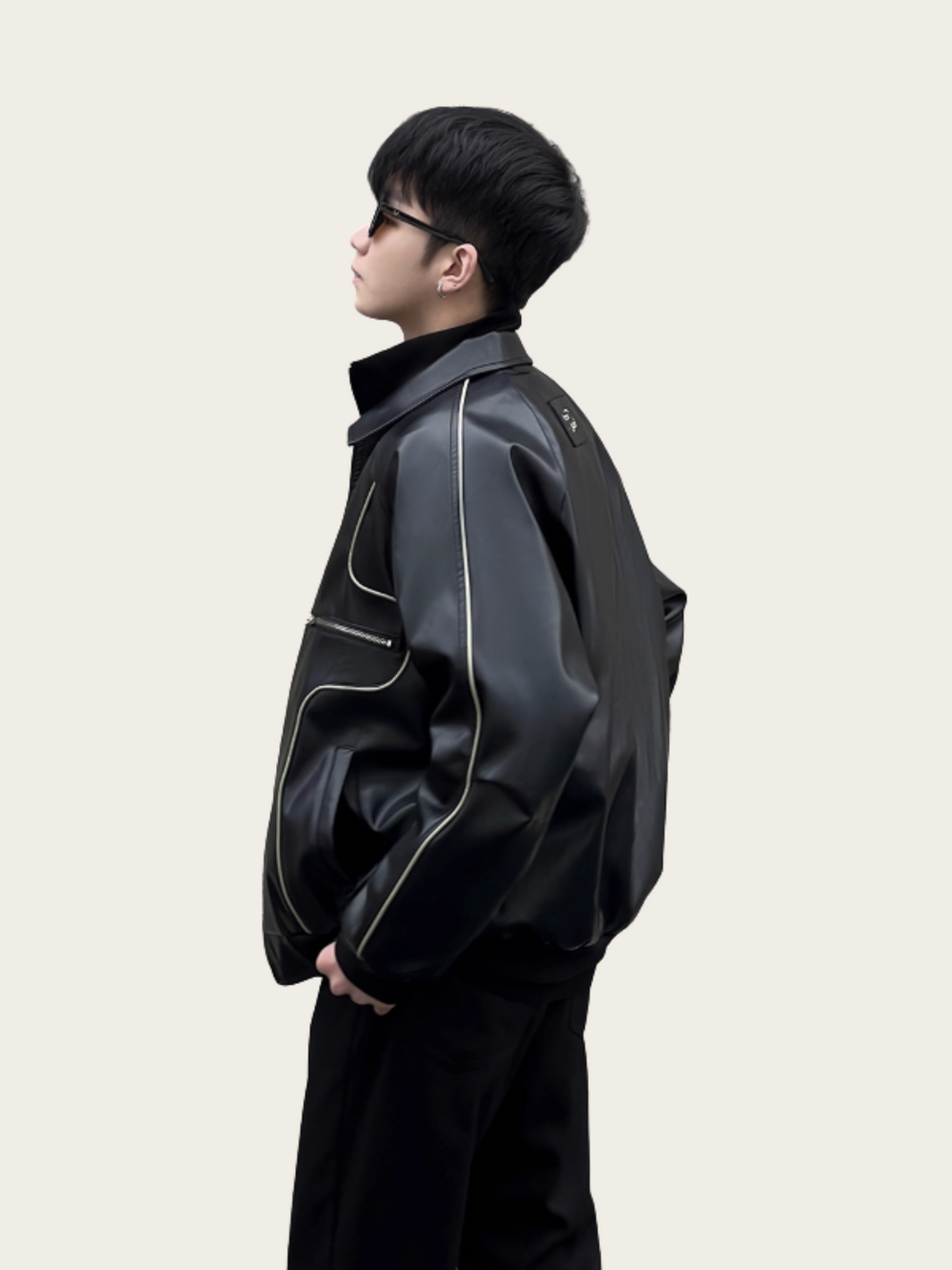 Person wearing a black leather jacket with white stitching on a plain background