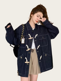 Person wearing a dark blue denim jacket with white buttons on a plain background