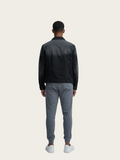 Man wearing a black jacket and gray pants on a beige background