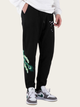 Person wearing black sweatpants with green peacock design and white sneakers on a light background