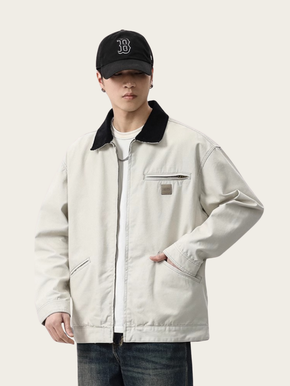 Person wearing a light-colored jacket with a black collar and a black cap on a white background