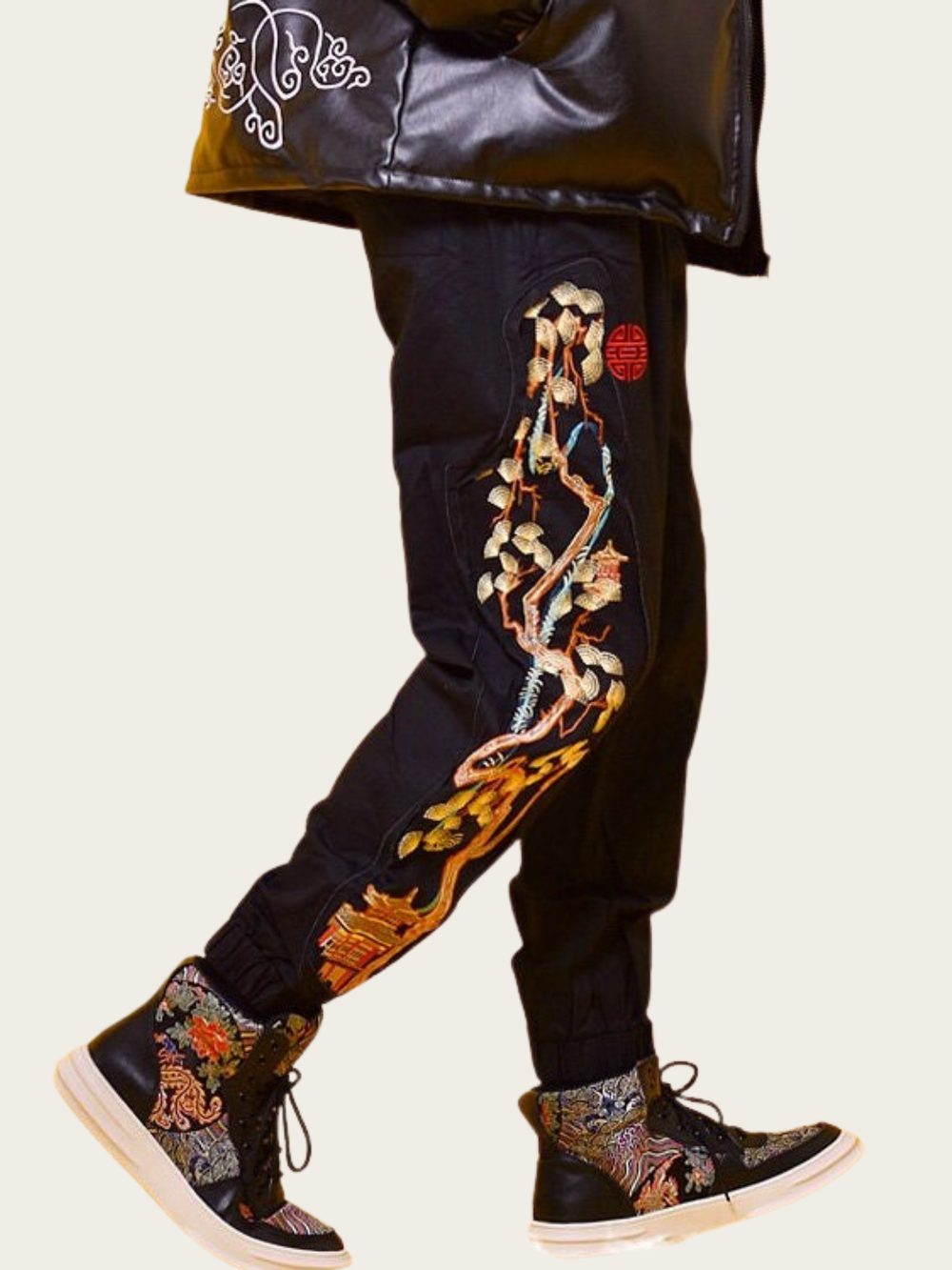 Black pants with colorful floral embroidery and a black jacket on a white background