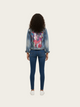 Person wearing a floral denim jacket and blue jeans on a white background