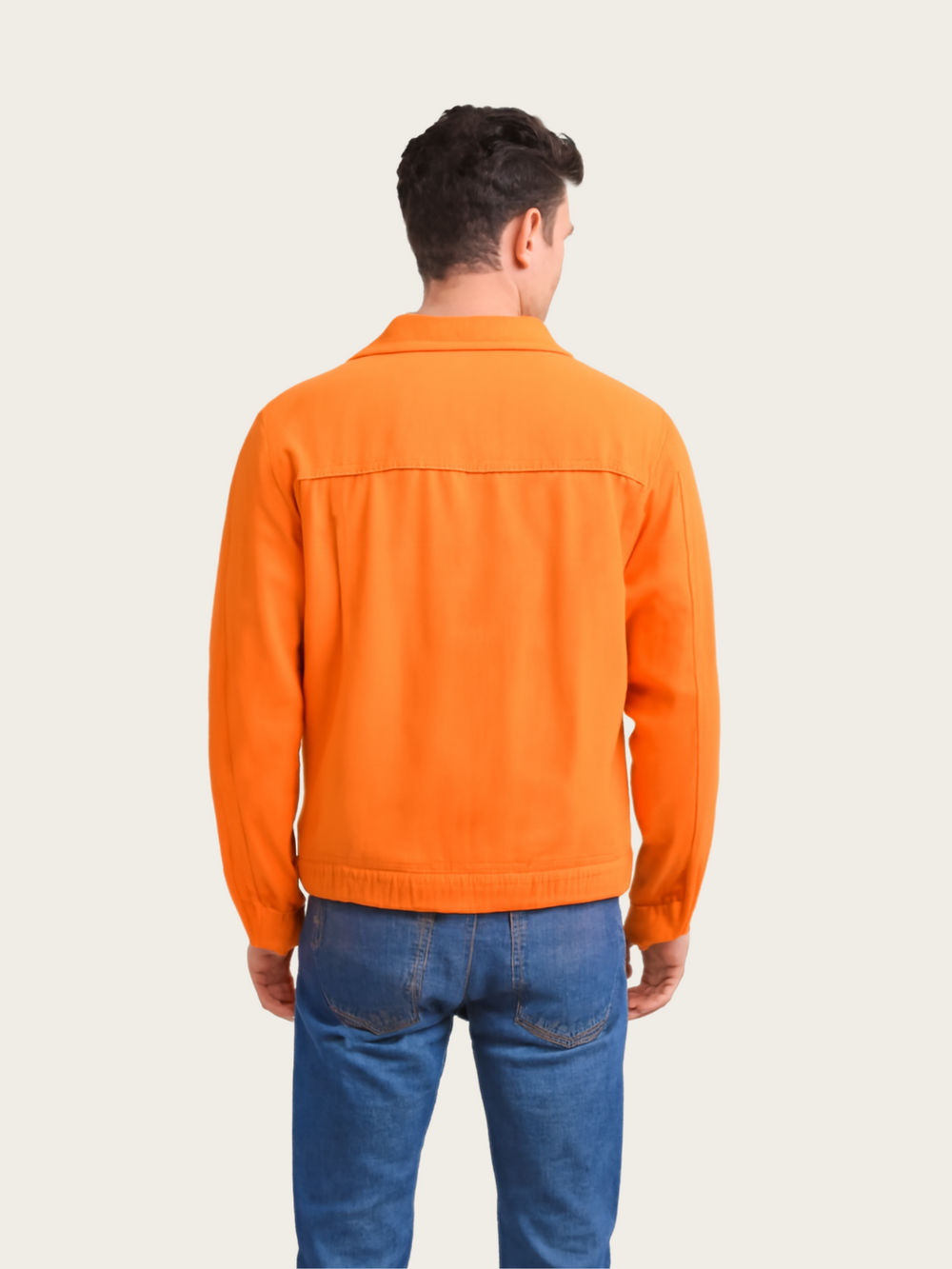 Person wearing an orange jacket and blue jeans on a plain background