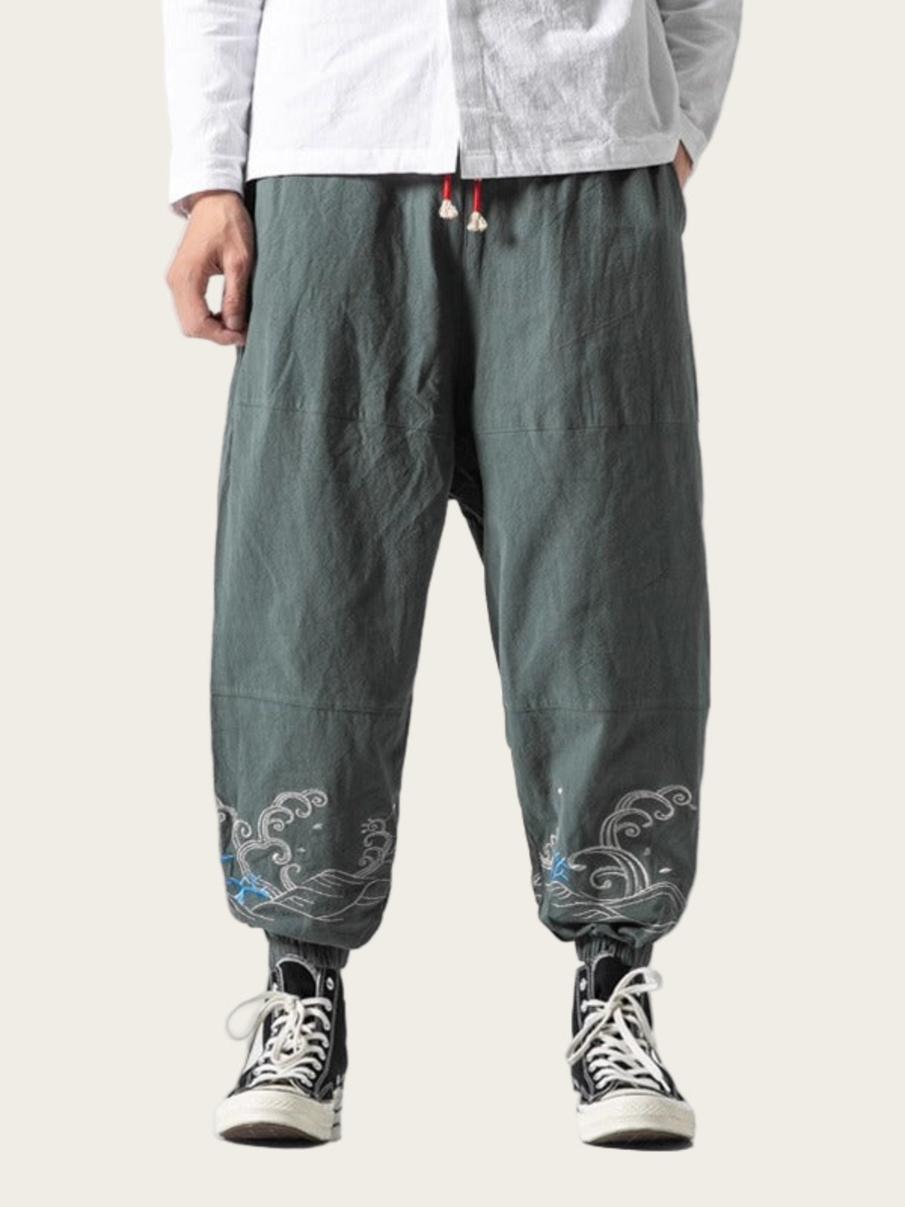 Person wearing green pants with floral embroidery on a plain background