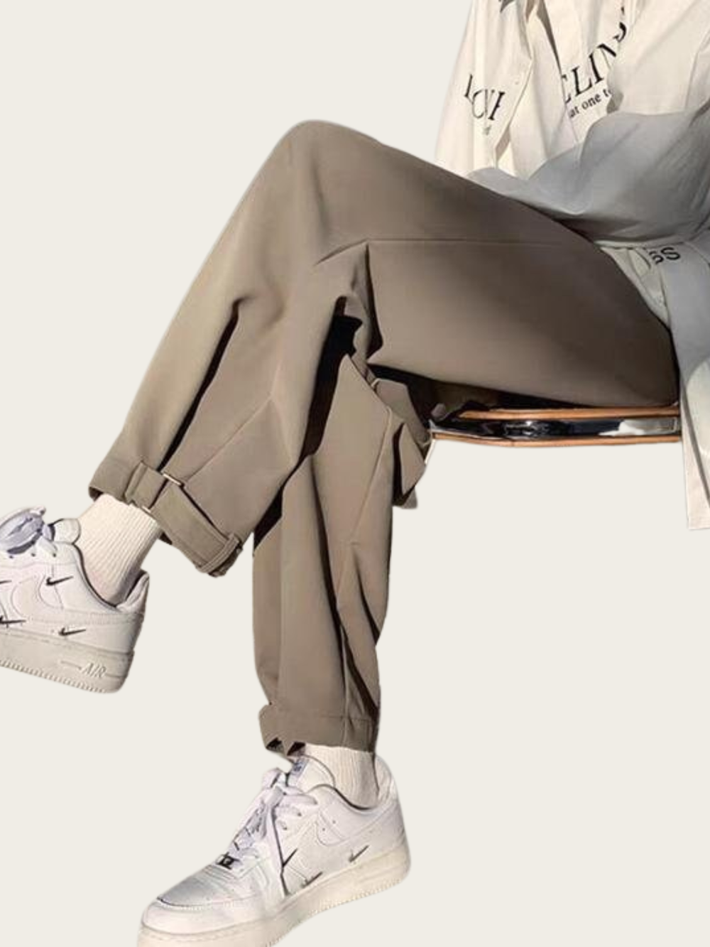 Person wearing beige pants and white sneakers sitting on a chair with a neutral background