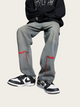Person wearing gray jeans with red accents and black sneakers on a beige background