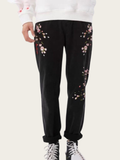 Black pants with floral embroidery worn by a person on a white background