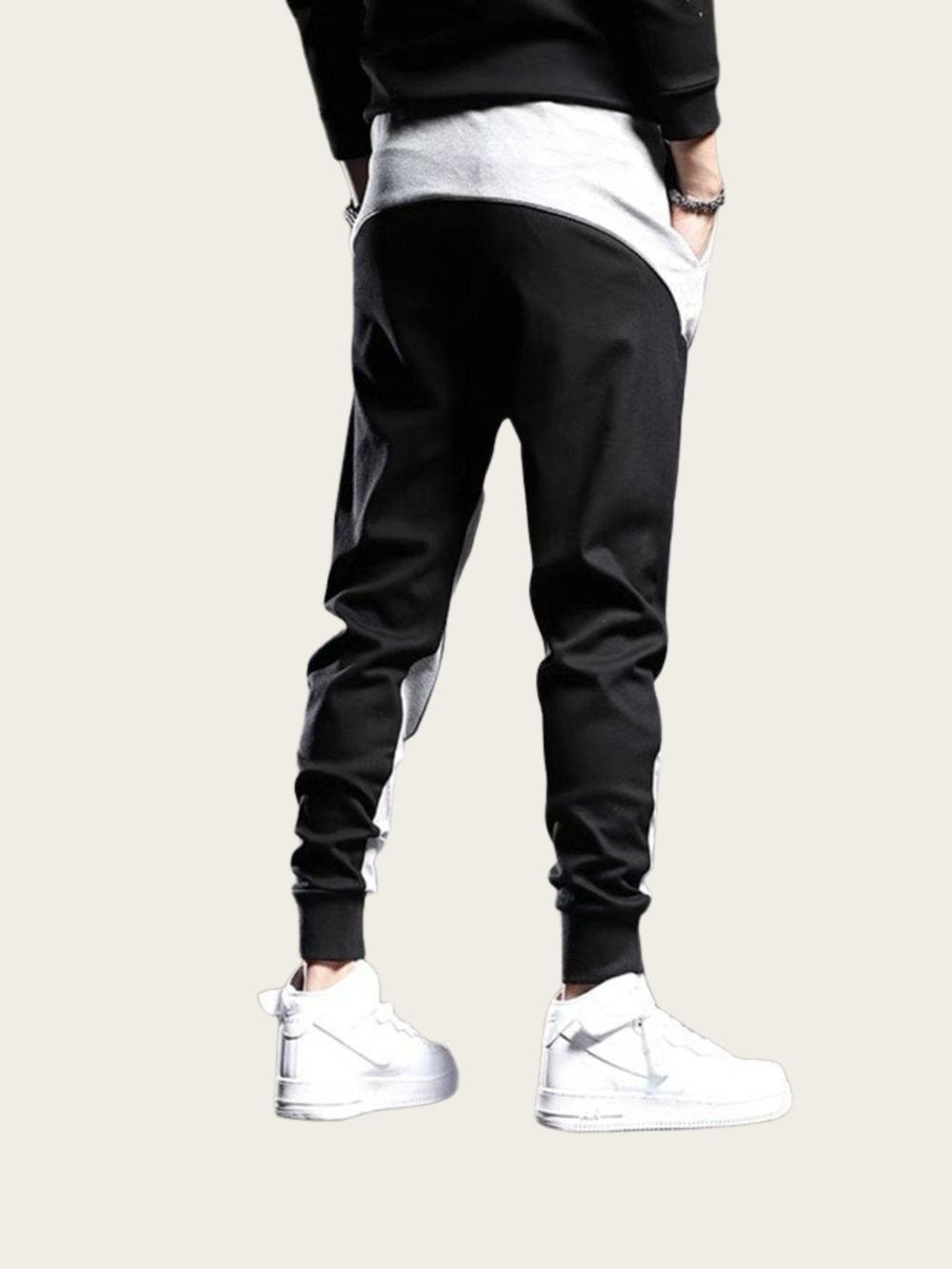 Person wearing black jogger pants and white sneakers on a light gray background