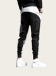 Person wearing black jogger pants and white sneakers on a light gray background