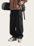 Person wearing a brown sweatshirt and black cargo pants holding a skateboard on a white background