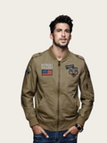 Man wearing a brown bomber jacket with patches on a beige background