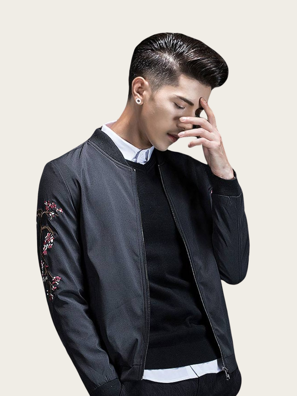 Man wearing a black bomber jacket with floral embroidery on a beige background