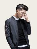 Man wearing a black bomber jacket with floral embroidery on a beige background