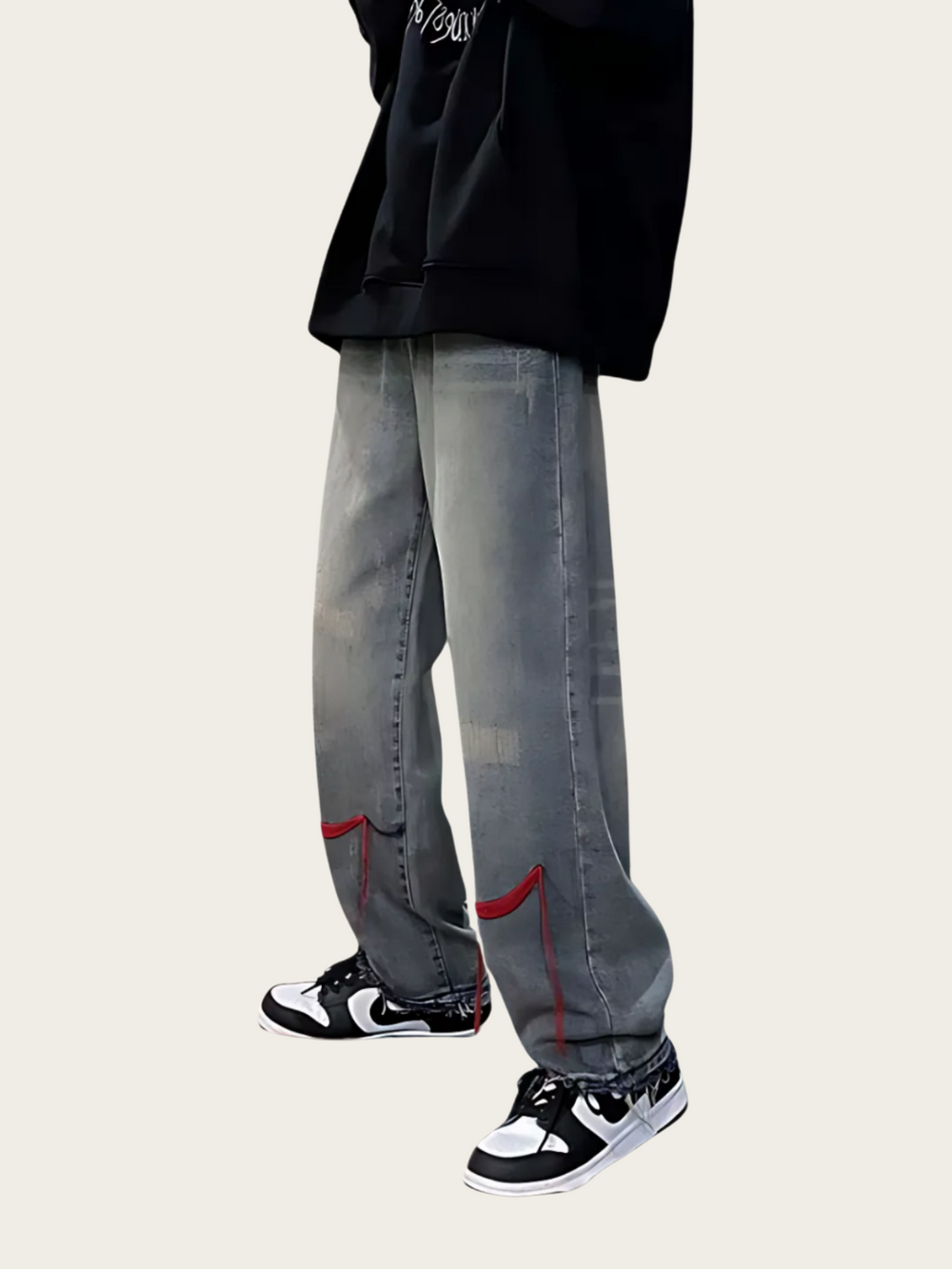 Person wearing gray jeans with red accents and black sneakers on a beige background