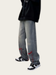 Person wearing gray jeans with red accents and black sneakers on a beige background