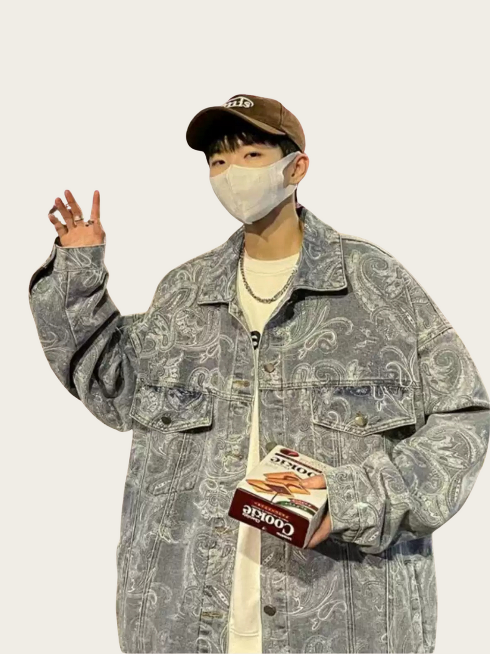 Person wearing a patterned jacket and cap, holding a box of cigarettes.