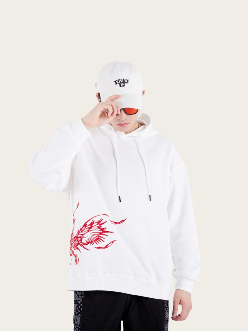 Person wearing a white hoodie with a red design and a white cap on a beige background