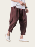 Person wearing brown harem pants and white shoes on a plain background