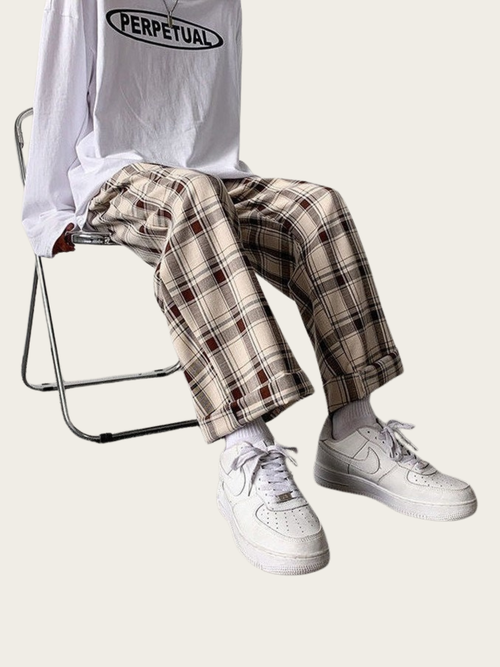 Person wearing a white 'PERPETUAL' t-shirt, plaid pants, and white sneakers sitting on a chair.