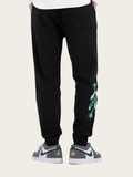 Black jogger pants with green design on a beige background