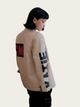 Person wearing a beige jacket with text on sleeves against a plain background