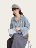Woman wearing a light blue denim jacket with floral patterns, holding a white clutch with blue accents.