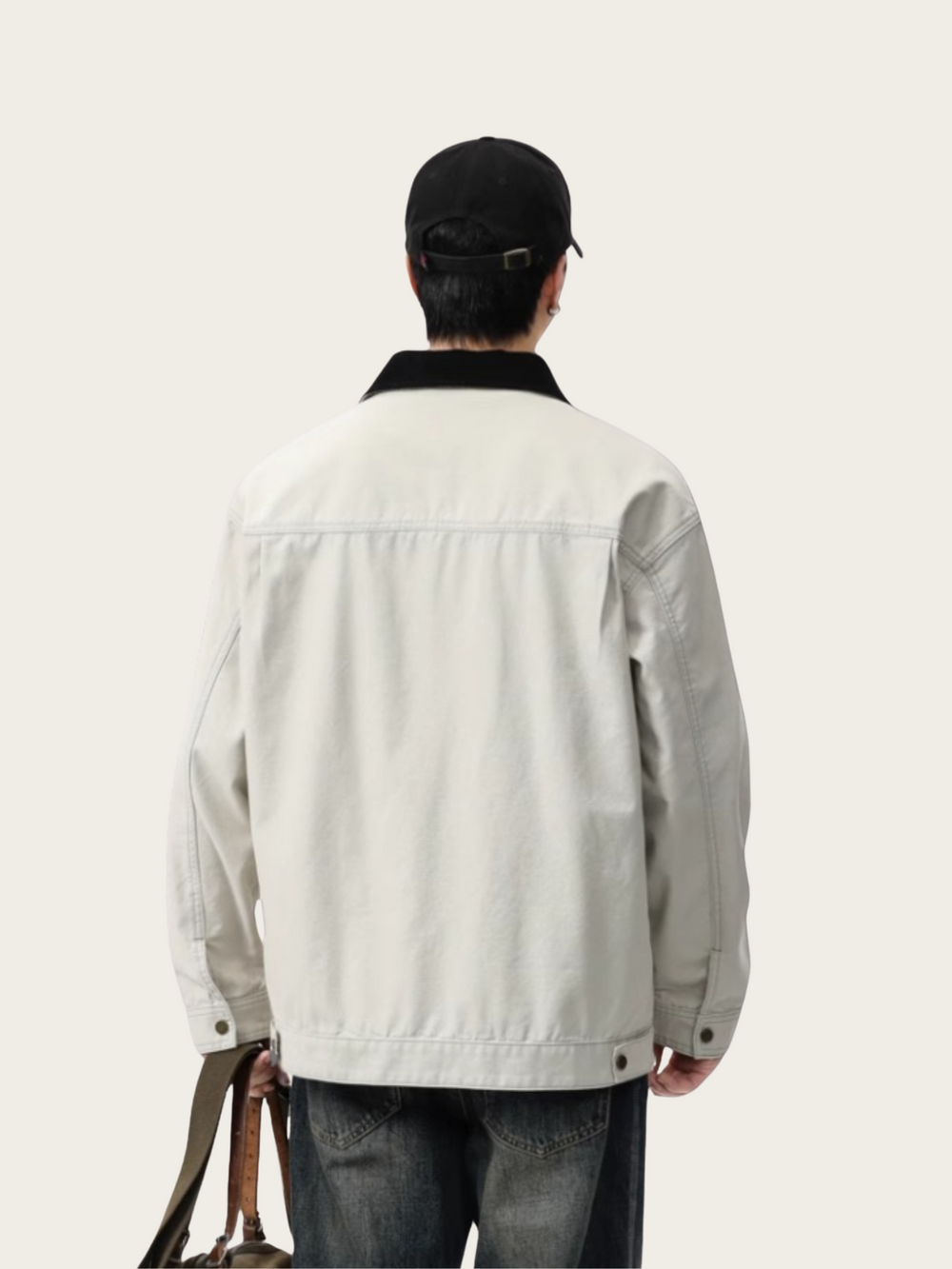 Person wearing a light-colored jacket and dark cap from behind on a plain background