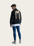 Person wearing a black jacket with a yellow logo on the back, standing against a plain background.