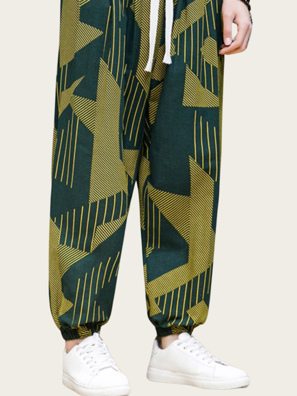 Green and yellow patterned pants worn with white sneakers on a beige background