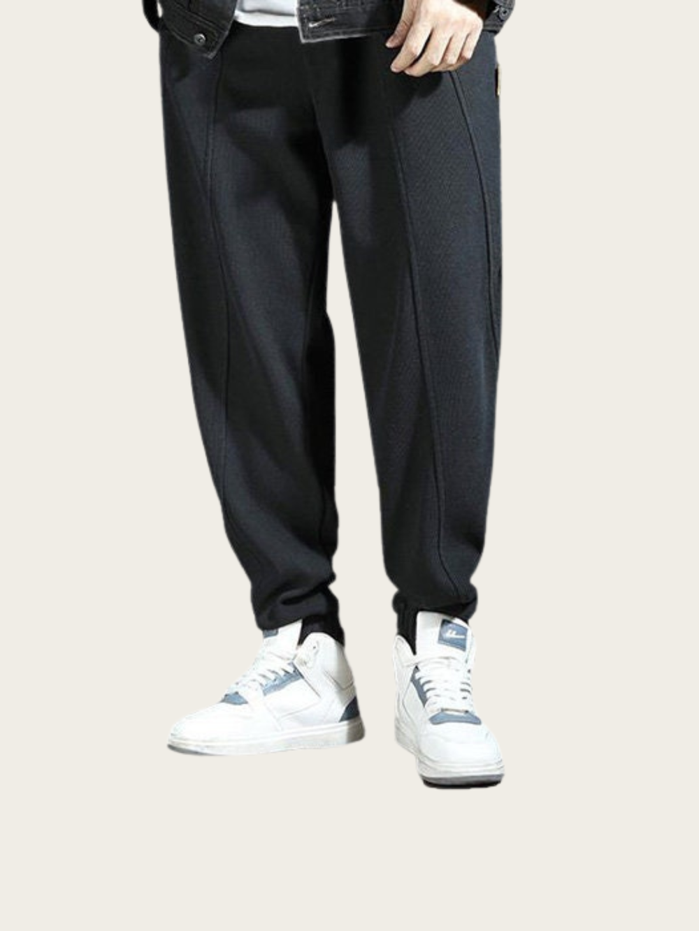 Person wearing black pants and white sneakers on a light gray background