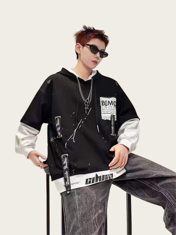 Person wearing a black and white hoodie with text and graphics, sitting on a chair against a plain background.