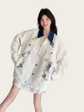 Woman wearing a white jacket with floral embroidery on a plain background