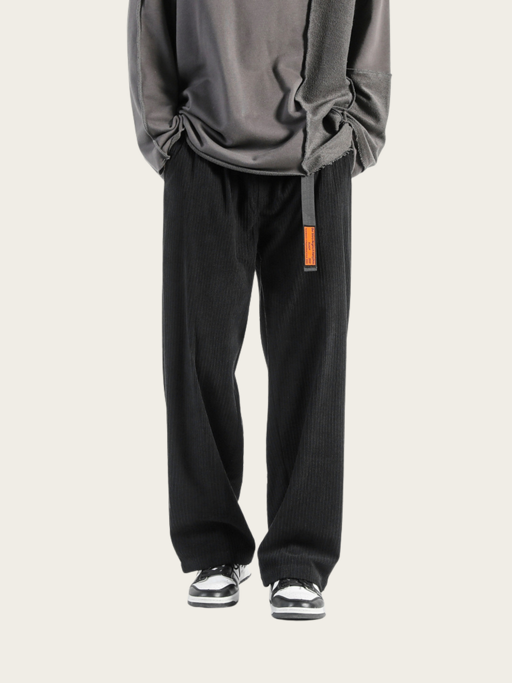 Person wearing a gray sweatshirt and black pants with an orange tag on a white background