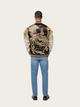 Person wearing a decorative jacket with a large bird design on a plain background