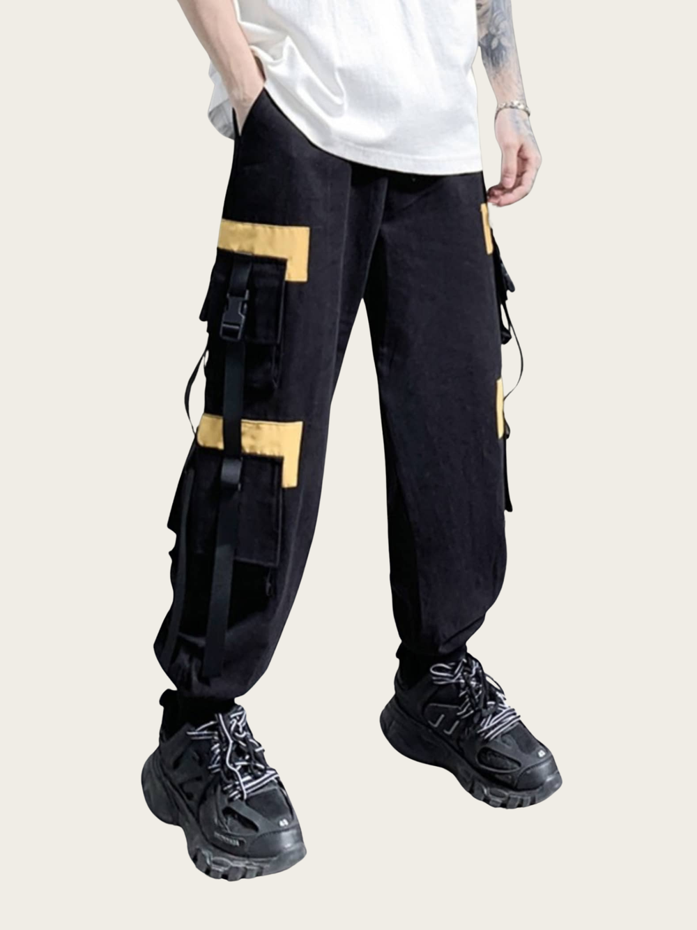 Person wearing black cargo pants with yellow accents and black sneakers on a beige background