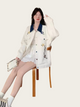 Woman wearing a white embroidered jacket sitting on a wooden stool against a white background