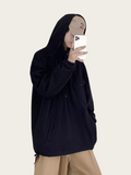 Person wearing a black hoodie and beige pants holding a phone on a plain background